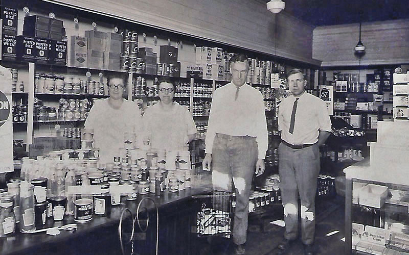 an old photo with four people standing in the grocery store